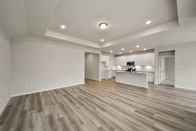 unfurnished living room featuring light wood-type flooring and a tray ceiling