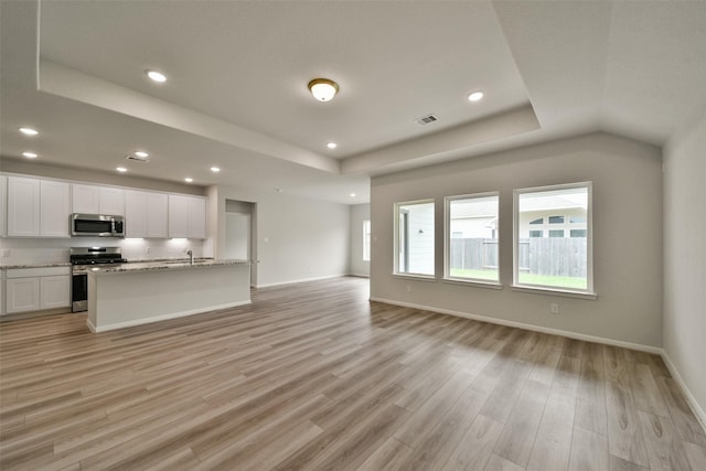 kitchen with light wood-type flooring, light stone counters, stainless steel appliances, a kitchen island with sink, and white cabinets