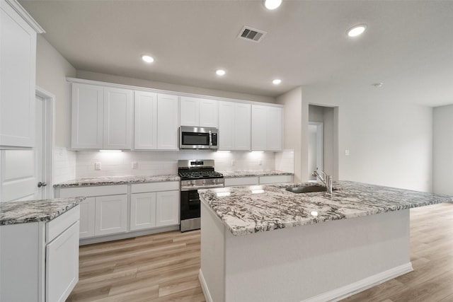 kitchen with white cabinetry, a center island with sink, light hardwood / wood-style flooring, and appliances with stainless steel finishes