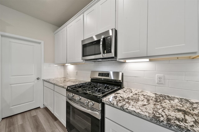 kitchen featuring light stone countertops, tasteful backsplash, appliances with stainless steel finishes, white cabinets, and light wood-type flooring