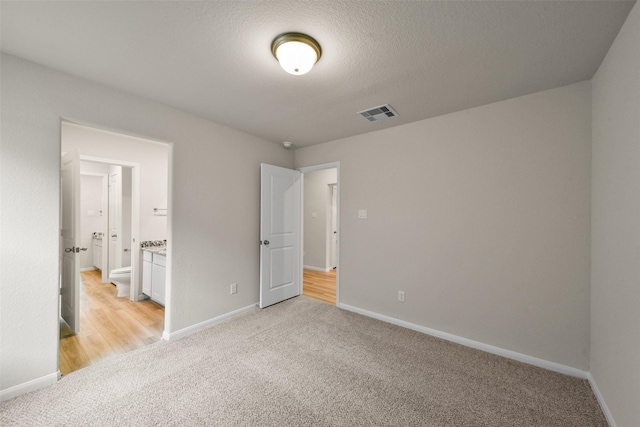 unfurnished bedroom with light carpet, a textured ceiling, and ensuite bathroom