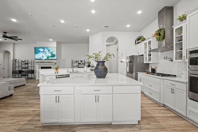 kitchen with wall chimney exhaust hood, stainless steel appliances, a kitchen island, light hardwood / wood-style floors, and white cabinets