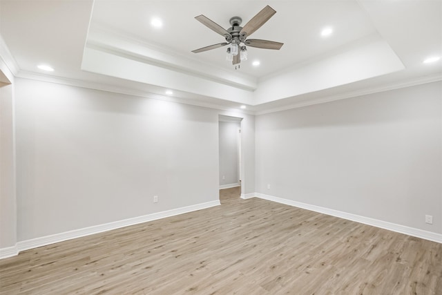 empty room with a raised ceiling, ornamental molding, and light wood-type flooring