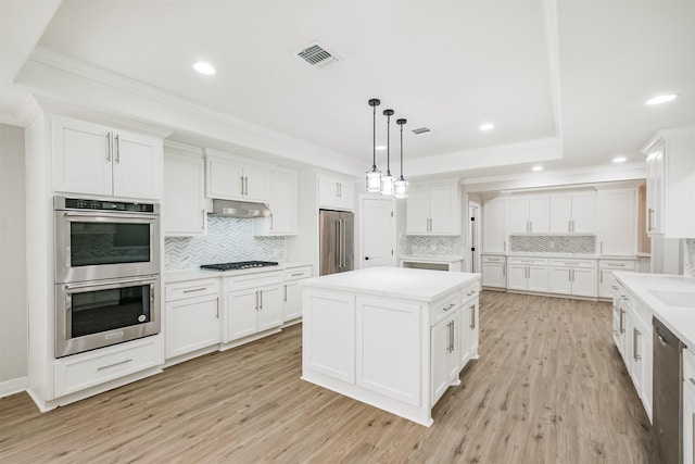 kitchen featuring appliances with stainless steel finishes, light wood-type flooring, white cabinetry, and hanging light fixtures