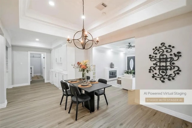 dining space with ceiling fan with notable chandelier, light wood-type flooring, a raised ceiling, and ornamental molding