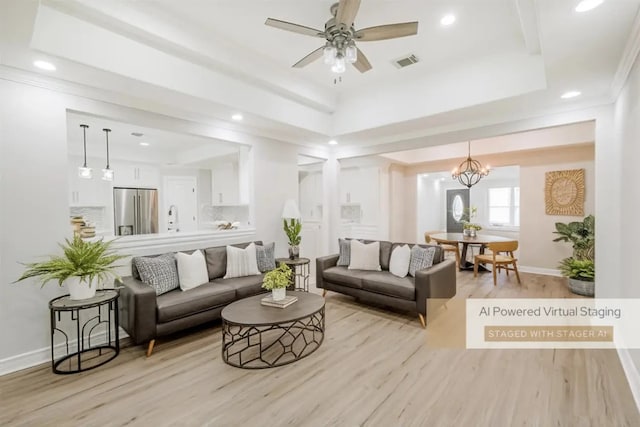 living room with ceiling fan with notable chandelier, light wood-type flooring, a raised ceiling, and sink