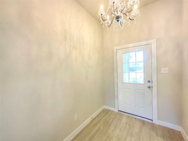 doorway with a notable chandelier, high vaulted ceiling, and light hardwood / wood-style flooring