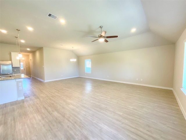 unfurnished room with ceiling fan with notable chandelier, light hardwood / wood-style floors, and vaulted ceiling