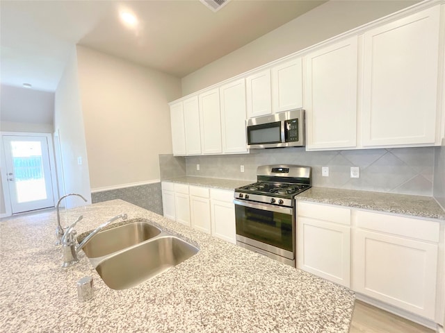 kitchen with light stone countertops, appliances with stainless steel finishes, backsplash, sink, and white cabinetry