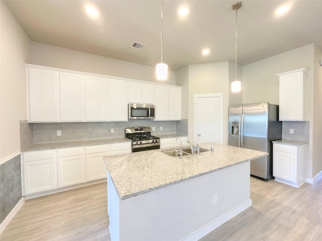 kitchen featuring decorative light fixtures, white cabinetry, an island with sink, and appliances with stainless steel finishes