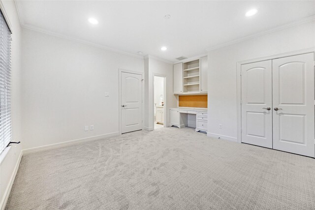 unfurnished bedroom featuring a closet, light colored carpet, ornamental molding, and built in desk