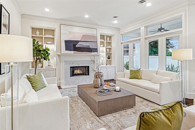 living room featuring ceiling fan, a premium fireplace, built in features, light hardwood / wood-style flooring, and crown molding