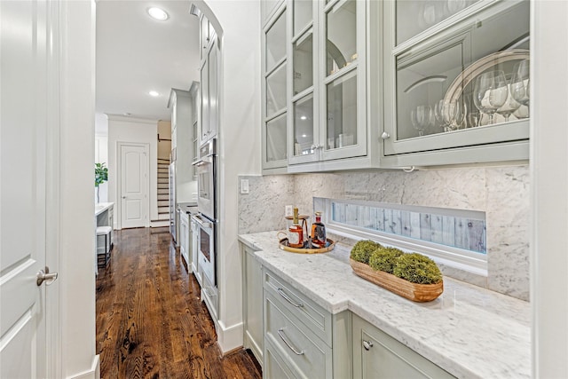 kitchen with light stone counters, double oven, dark wood-type flooring, and tasteful backsplash