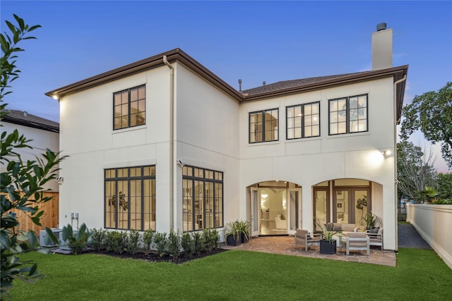 back house at dusk with a lawn, a patio area, and an outdoor living space