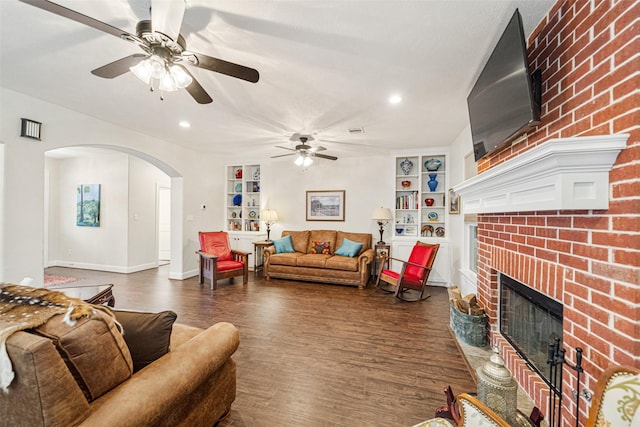 living room with built in shelves, dark hardwood / wood-style floors, a brick fireplace, and ceiling fan