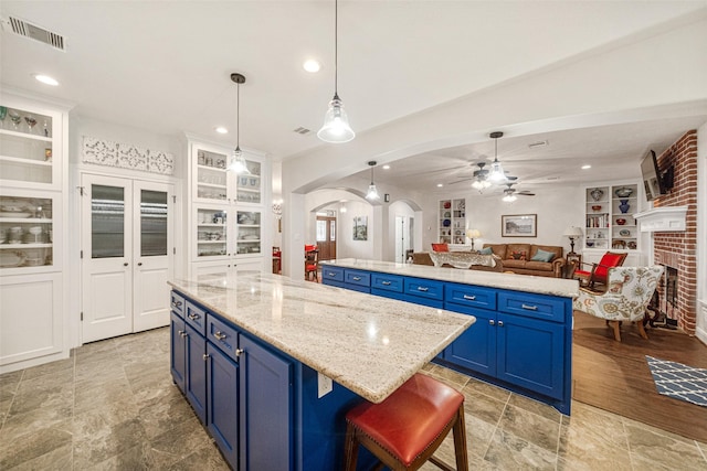 kitchen featuring blue cabinetry, a center island, hanging light fixtures, a brick fireplace, and a breakfast bar