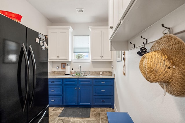 kitchen with blue cabinetry, white cabinets, black fridge, and sink