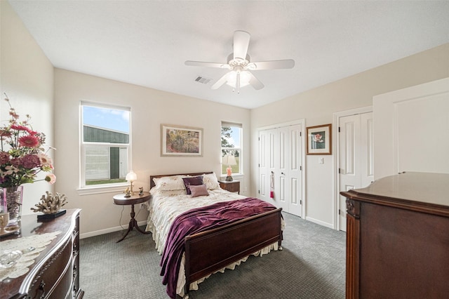 bedroom featuring dark colored carpet, ceiling fan, multiple closets, and multiple windows