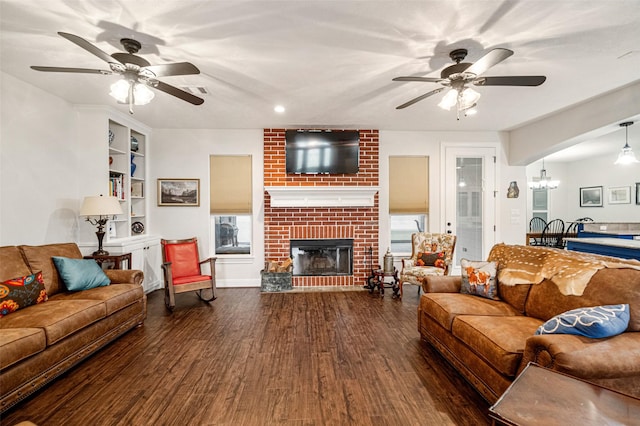 living room with a fireplace, ceiling fan with notable chandelier, dark wood-type flooring, and built in features