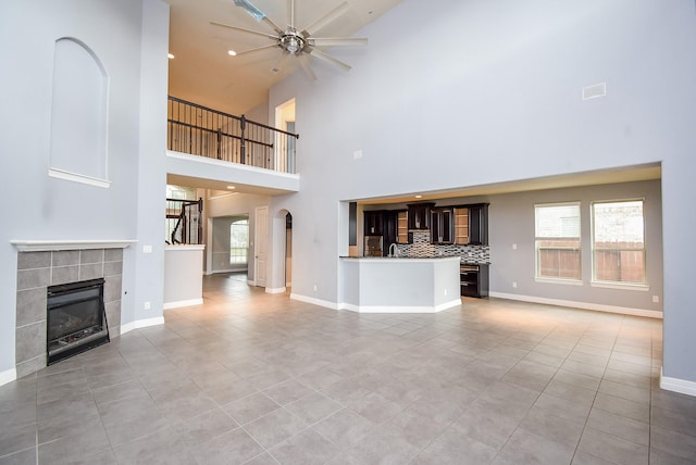 unfurnished living room with ceiling fan, light tile patterned flooring, a fireplace, and high vaulted ceiling