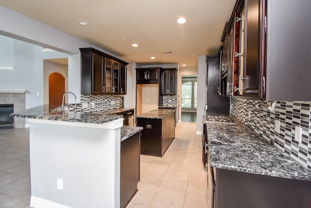 kitchen featuring decorative backsplash, a kitchen island, dark stone countertops, and light tile patterned floors