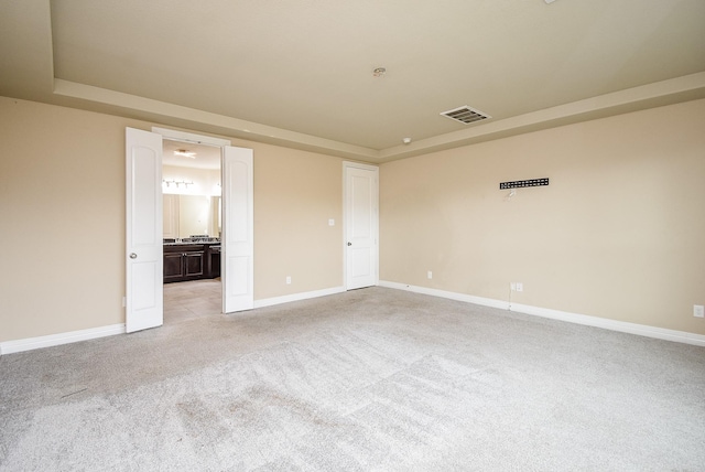 empty room featuring a tray ceiling and light colored carpet