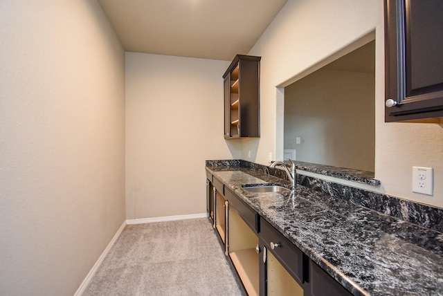 kitchen with light carpet, dark brown cabinetry, dark stone countertops, and sink