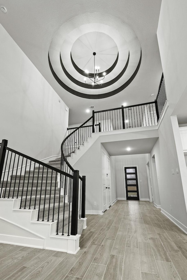 entryway featuring a raised ceiling, light hardwood / wood-style flooring, a towering ceiling, and a chandelier