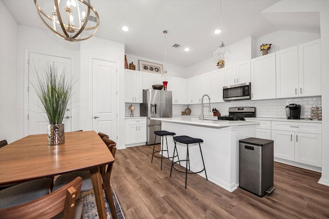 kitchen featuring pendant lighting, dark wood-type flooring, stainless steel appliances, and an island with sink