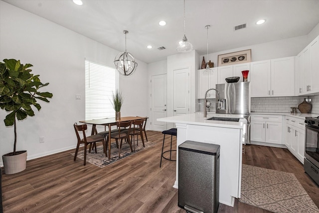 kitchen featuring white cabinets, decorative light fixtures, dark hardwood / wood-style flooring, and an island with sink