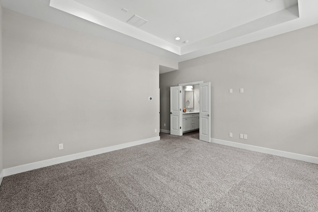 unfurnished bedroom with carpet, connected bathroom, and a tray ceiling