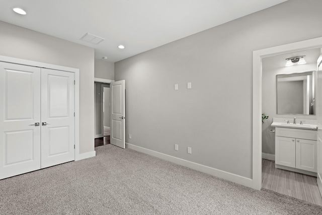 unfurnished bedroom with sink, light colored carpet, a closet, and ensuite bathroom