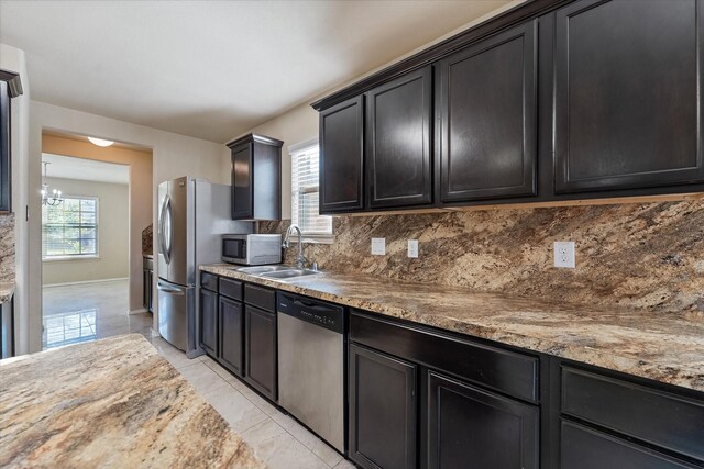 kitchen featuring decorative backsplash, light stone counters, stainless steel appliances, sink, and a chandelier