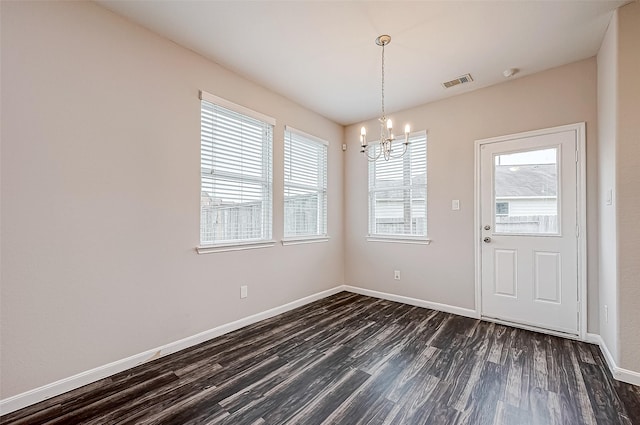 unfurnished dining area with a healthy amount of sunlight, dark hardwood / wood-style flooring, and an inviting chandelier