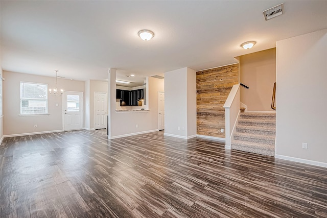 unfurnished living room with wooden walls, dark hardwood / wood-style flooring, and a chandelier