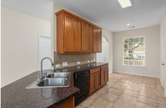 kitchen featuring dishwasher, dark stone counters, sink, light tile patterned floors, and tasteful backsplash