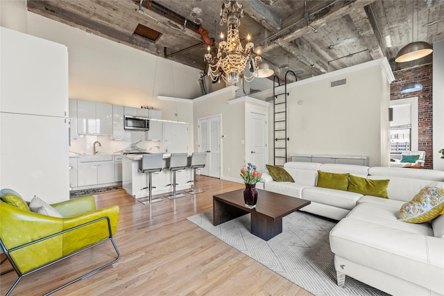 living room with a high ceiling, light hardwood / wood-style floors, a notable chandelier, and sink