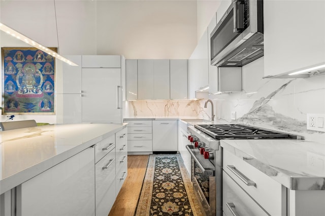 kitchen featuring sink, light hardwood / wood-style flooring, appliances with stainless steel finishes, tasteful backsplash, and white cabinetry