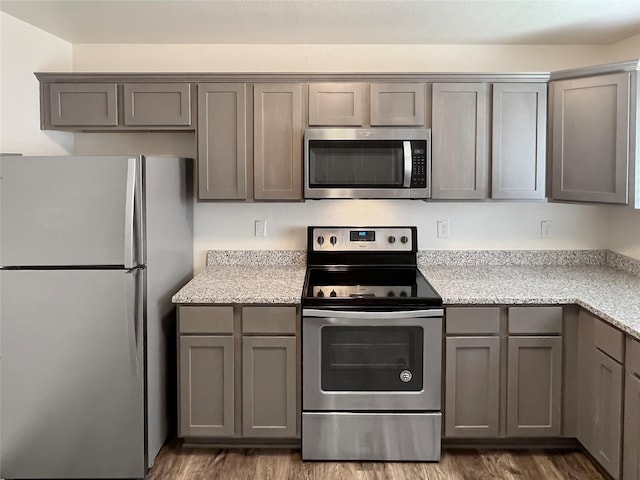 kitchen featuring gray cabinets, light stone counters, dark hardwood / wood-style flooring, and appliances with stainless steel finishes