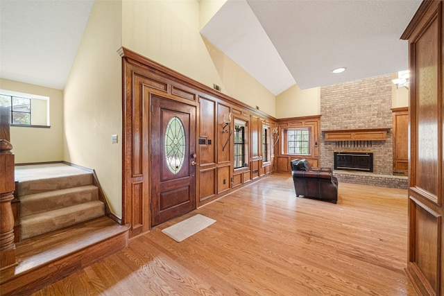 foyer with a fireplace, light wood-type flooring, and lofted ceiling