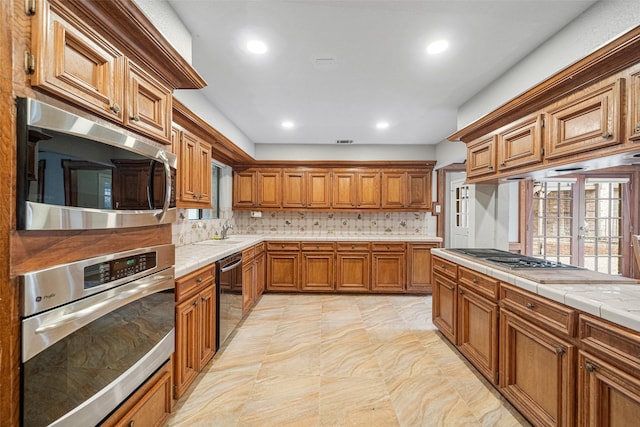 kitchen featuring tile counters, decorative backsplash, sink, and appliances with stainless steel finishes