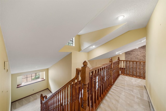 hall featuring a textured ceiling, light colored carpet, and lofted ceiling