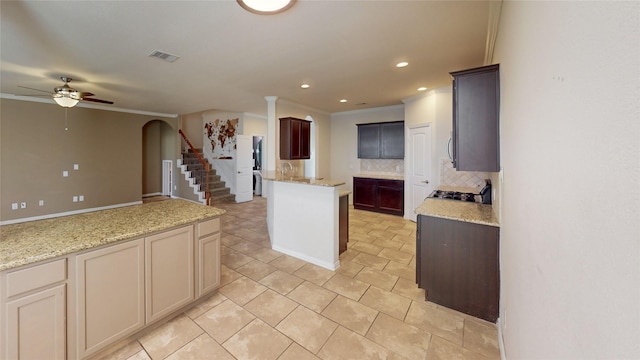 kitchen featuring decorative backsplash, light stone countertops, ceiling fan, crown molding, and a kitchen island