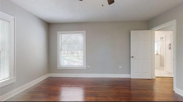 empty room with a wealth of natural light, ceiling fan, and dark wood-type flooring