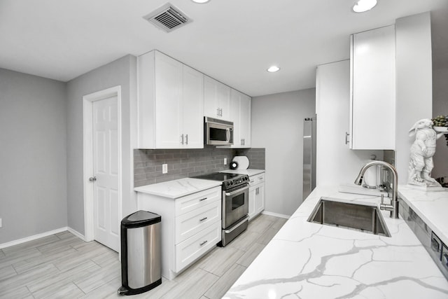 kitchen featuring sink, decorative backsplash, light stone counters, white cabinetry, and stainless steel appliances