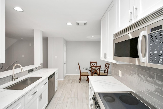 kitchen with tasteful backsplash, light stone counters, stainless steel appliances, sink, and white cabinetry