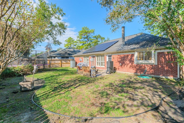 rear view of house featuring solar panels, a patio area, a lawn, and a trampoline