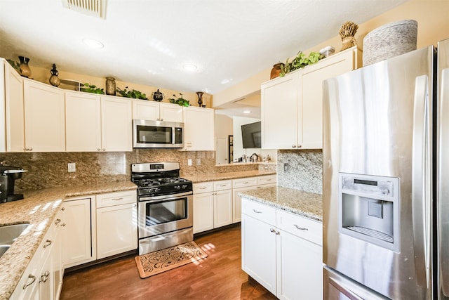 kitchen with decorative backsplash, appliances with stainless steel finishes, white cabinetry, and dark wood-type flooring