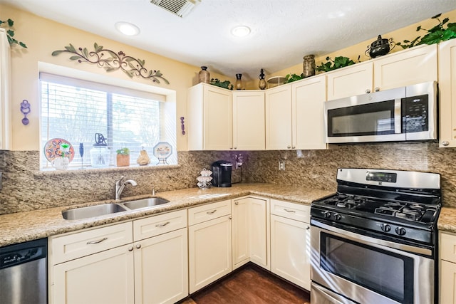 kitchen with decorative backsplash, stainless steel appliances, light stone countertops, and sink