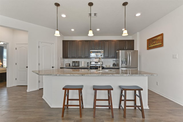 kitchen with sink, backsplash, a kitchen island with sink, dark brown cabinets, and appliances with stainless steel finishes